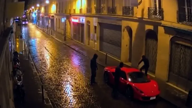 Hooded guys climb all over a red supercar in the rain